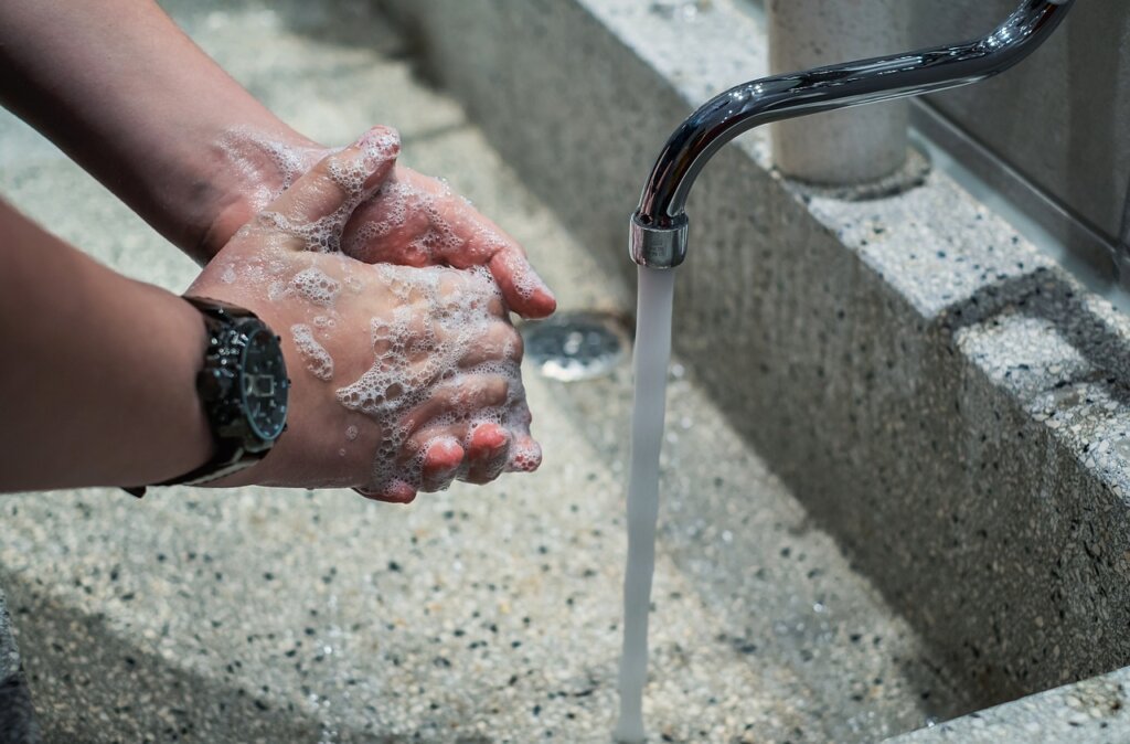 person rinsing air conditioner filter under running water gently