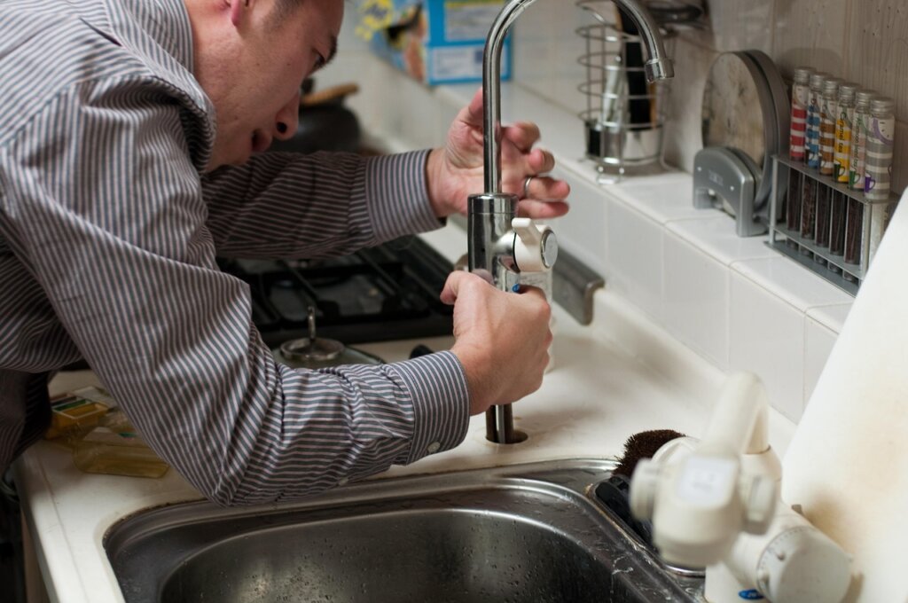 professional plumber inspecting under kitchen sink with flashlight