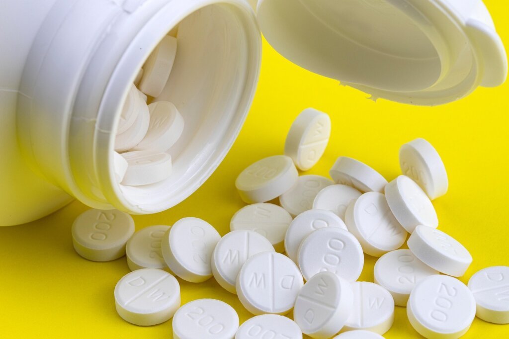 person holding stomach with vitamin supplement nearby